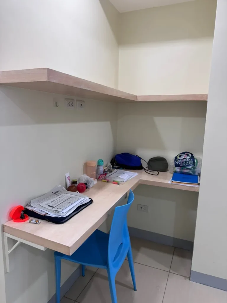 필리핀 세부 셀라(CELLA) 유니캠퍼스 어학원 기숙사 1인실로, 상단 선반과 L자형 책상에 교재·소지품이 정리된 코너 학습공간입니다.