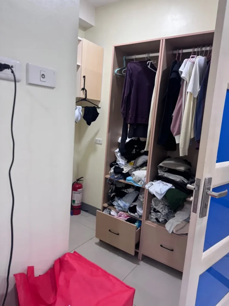 필리핀 세부 셀라(CELLA) 유니캠퍼스 어학원 기숙사 2인실로, 옷걸이 봉과 서랍이 갖춰진 붙박이 옷장에 의류가 정리되어 있습니다.