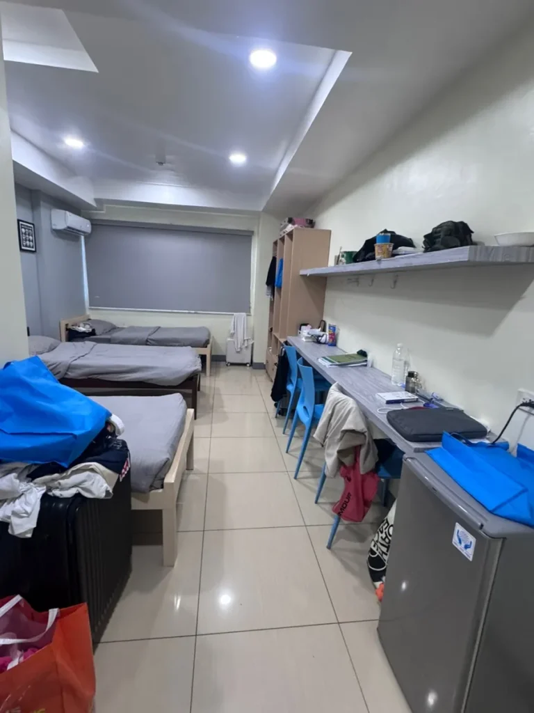 필리핀 세부 셀라(CELLA) 유니캠퍼스 어학원 기숙사 3인실로, 침대 3개와 원목 옷장·책상·미니냉장고·에어컨이 갖춰진 넓은 침실 전체 모습입니다.