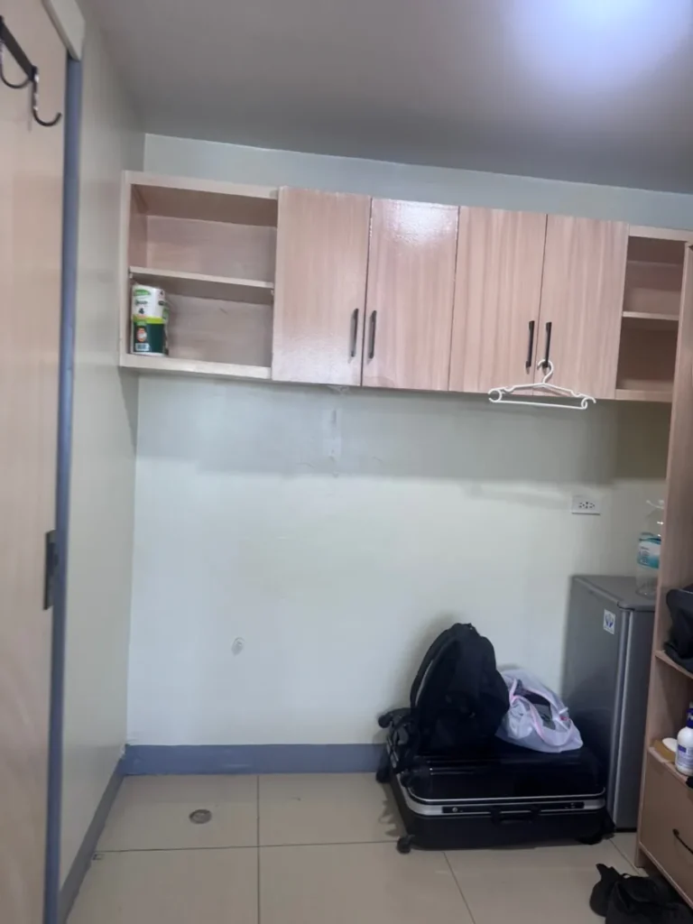 필리핀 세부 셀라(CELLA) 유니캠퍼스 어학원 기숙사 3인실로, 문 닫힌 벽 상부 캐비닛과 바닥의 캐리어·백팩·냉장고가 보이는 수납 코너입니다.