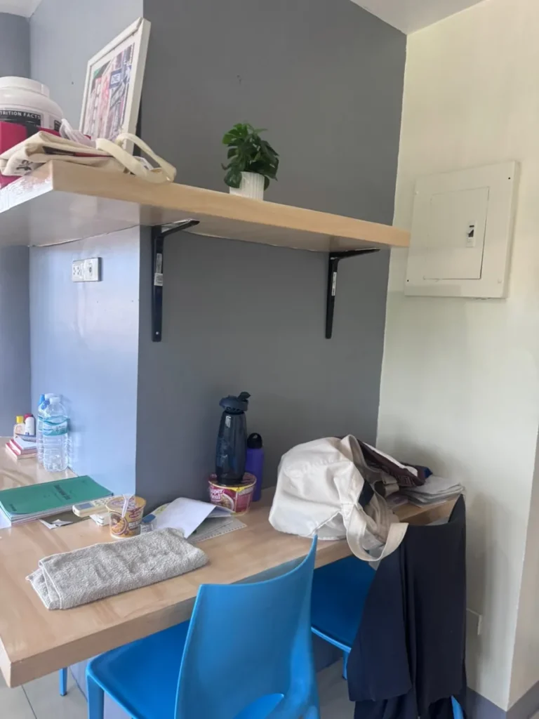 필리핀 세부 셀라(CELLA) 유니캠퍼스 어학원 기숙사 4인실 책상으로, 선반 위 화분과 액자, 책상 위에 생수병과 개인 소지품이 놓여 있습니다.