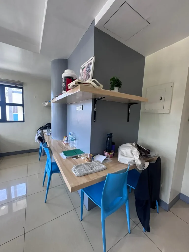 필리핀 세부 셀라(CELLA) 유니캠퍼스 어학원 기숙사 4인실로, 파란 의자 두 개가 놓인 책상 옆으로 창문이 보이는 학습 공간입니다.