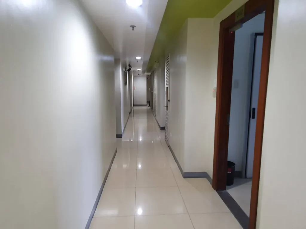 필리핀 세부 셀라(CELLA) 유니캠퍼스 어학원 기숙사 복도로, 초록색 포인트 천장 아래 객실 문들이 늘어선 깔끔한 타일 바닥의 긴 복도입니다.