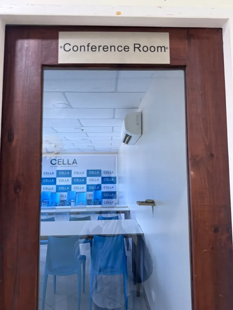 필리핀 세부 셀라(CELLA) 유니캠퍼스 어학원 강의실 컨퍼런스룸으로, 'Conference Room' 문패 너머로 CELLA 배경막이 보입니다.