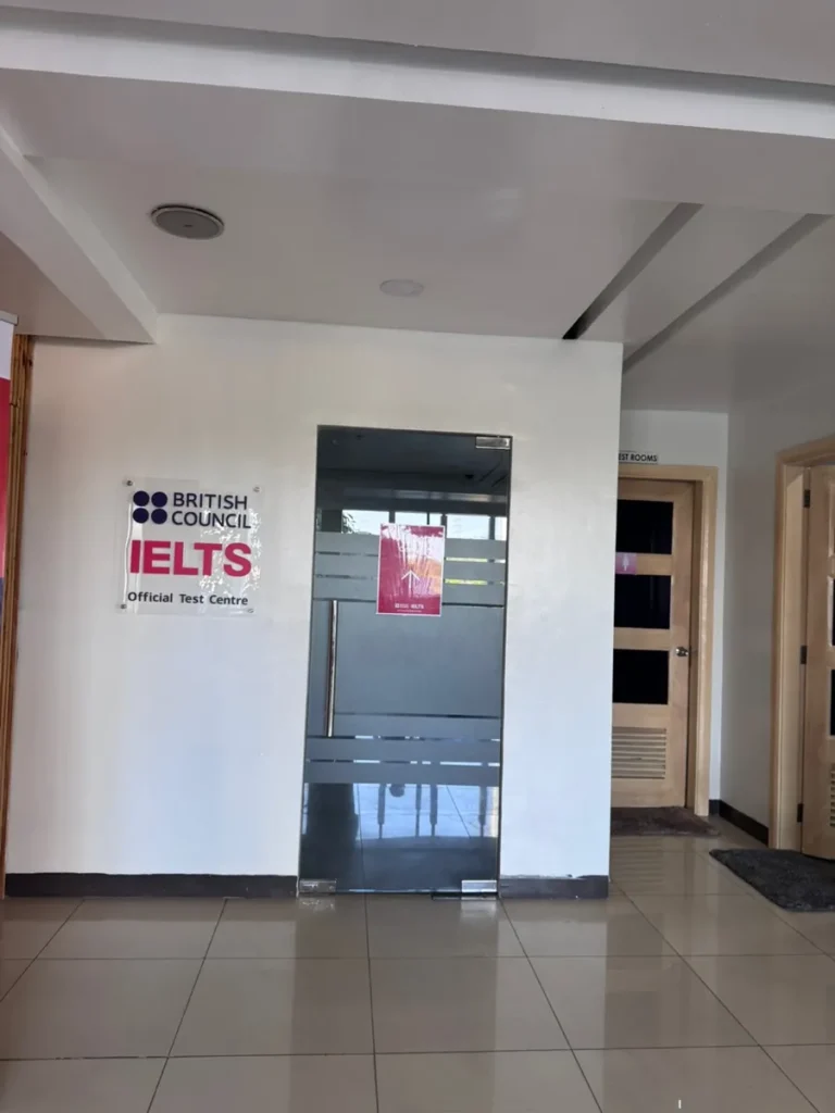 필리핀 세부 셀라(CELLA) 유니캠퍼스 어학원 강의실 아이엘츠 시험장으로, 브리티시카운슬 공식 시험장 안내판과 유리문이 있는 복도 입구입니다.