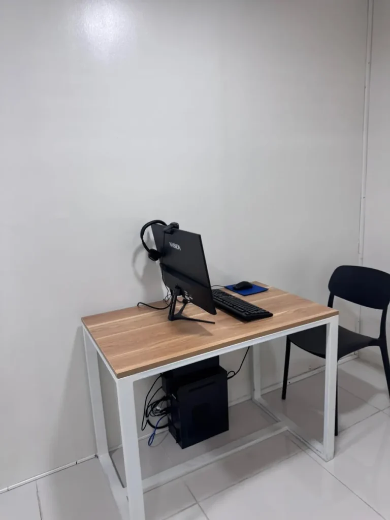 필리핀 세부 셀라(CELLA) 유니캠퍼스 어학원 강의실 아이엘츠 시험장으로, 원목 상판 책상에 모니터와 헤드셋·키보드가 놓인 개별 시험 좌석입니다.