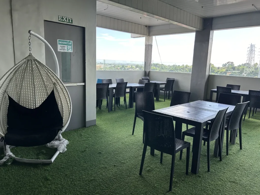 필리핀 세부 셀라(CELLA) 유니캠퍼스 어학원 부대시설 휴게공간으로, 비상구 옆 흰 라탄 소재 달걀 모양 그네의자와 테이블이 보이는 모습입니다.