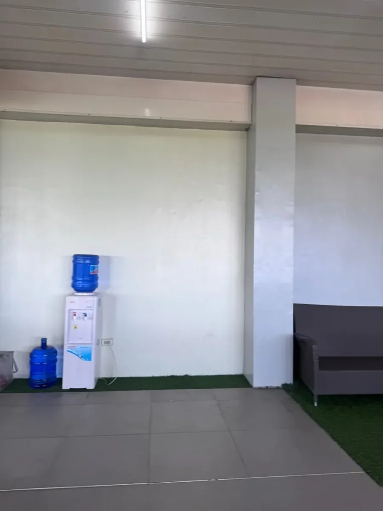 필리핀 세부 셀라(CELLA) 유니캠퍼스 어학원 부대시설 휴게공간으로, 생수통 정수기 옆 타일 바닥에 짙은 회색 소파가 놓인 휴게공간입니다.