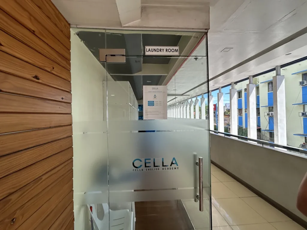 필리핀 세부 셀라(CELLA) 유니캠퍼스 어학원 부대시설 세탁실로, CELLA 로고가 새겨진 유리문에 라운드리룸 표지판이 붙은 입구입니다.