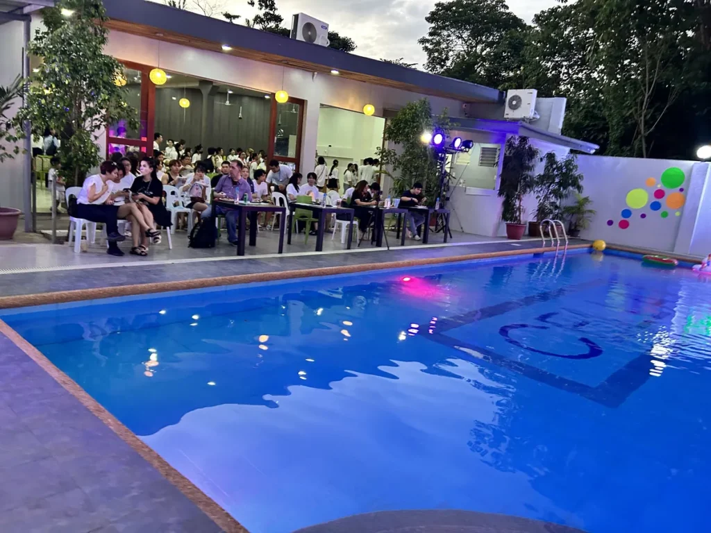 필리핀 세부 셀라(CELLA) 유니캠퍼스 어학원 운동시설 수영장으로, 해질녘 파빌리온에 학생들이 모여 앉고 조명이 비친 수영장이 보이는 모습입니다.