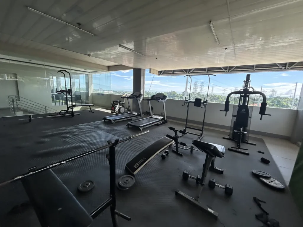 필리핀 세부 셀라(CELLA) 유니캠퍼스 어학원 운동시설 헬스장으로, 도심 전망이 펼쳐진 오픈에어 루프탑에 러닝머신·멀티짐이 배치된 공간입니다.