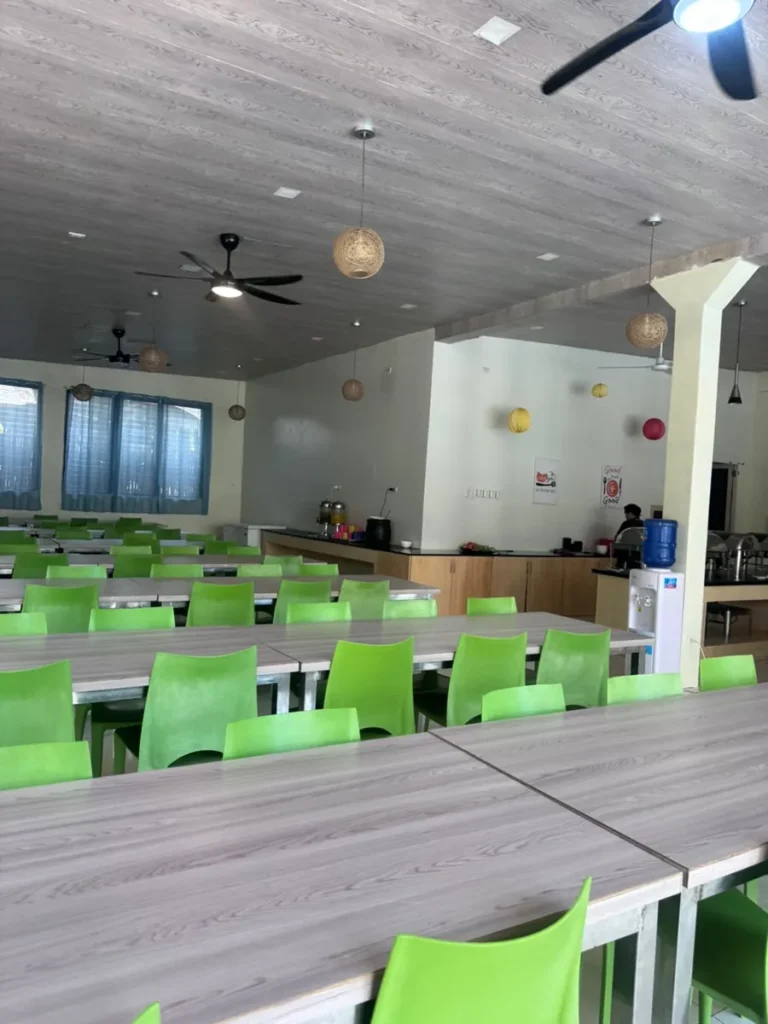 필리핀 세부 셀라(CELLA) 유니캠퍼스 어학원 식당으로, 알록달록한 전등 장식과 정수기가 놓인 배식대 쪽으로 초록 의자 테이블이 이어집니다.