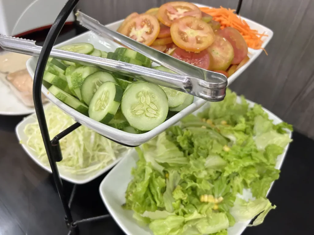 필리핀 세부 셀라(CELLA) 유니캠퍼스 어학원 학생식당 식사로, 오이·토마토·당근·양상추가 3단 스탠드에 나뉘어 담긴 샐러드바 모습입니다.