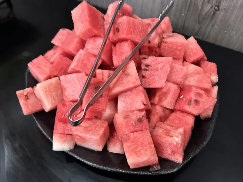 필리핀 세부 셀라(CELLA) 유니캠퍼스 어학원 학생식당 식사로, 씨앗이 보이는 붉은 수박 조각이 검은 접시 위에 집게와 함께 수북이 쌓인 모습입니다.