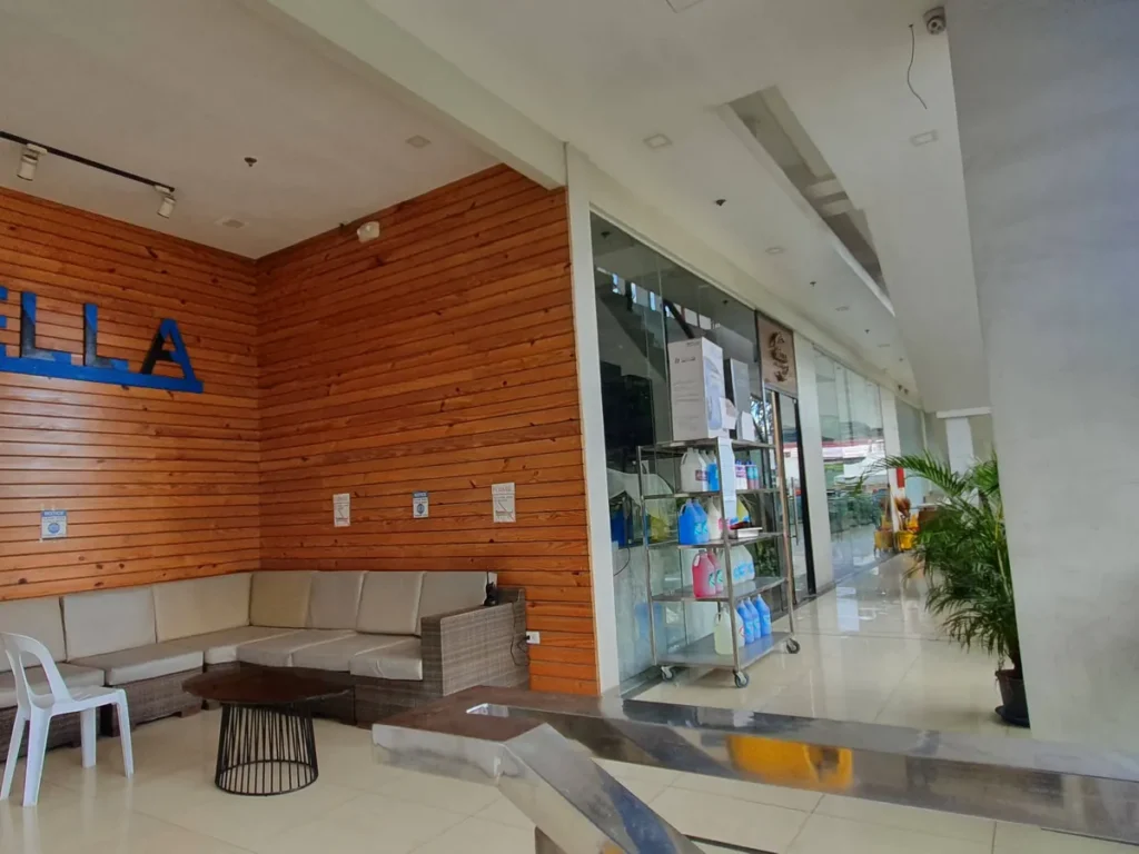 필리핀 세부 셀라(CELLA) 유니캠퍼스 어학원 학원전경 입구로비로, 청소용 카트와 소파가 놓이고 통유리 너머 바깥이 보이는 로비 안쪽 통로입니다.