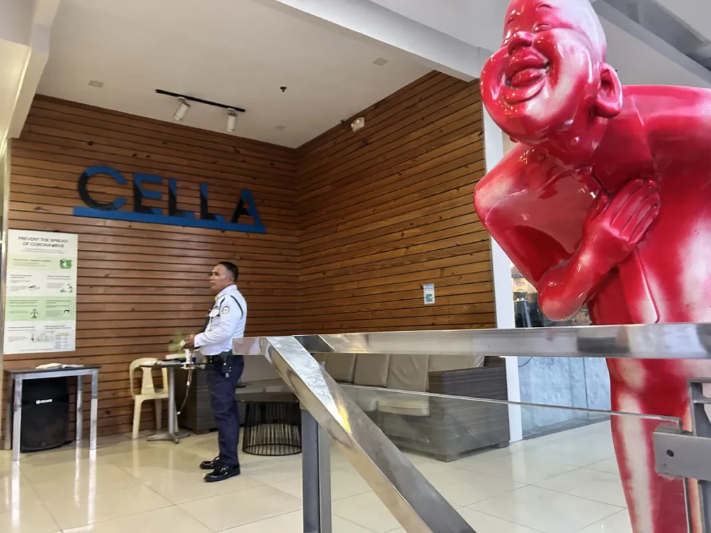 필리핀 세부 셀라(CELLA) 유니캠퍼스 어학원 학원전경 입구로비로, CELLA 로고 벽 앞 경비원과 붉은 복돼지 조형물이 있는 로비 전경입니다.