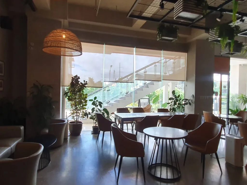 필리핀 세부 셀라(CELLA) 유니캠퍼스 어학원 주변시설 카페로, 통유리 너머 외부 계단이 내다보이는 대리석 원형 테이블과 가죽 의자 좌석입니다.