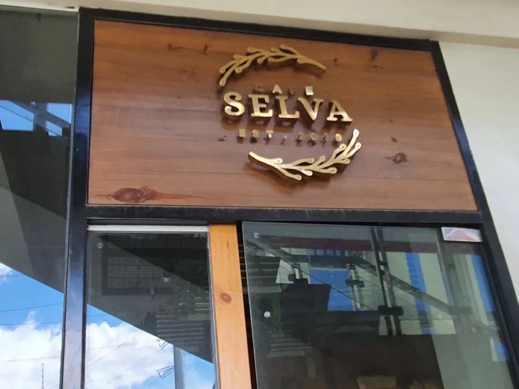 필리핀 세부 셀라(CELLA) 유니캠퍼스 어학원 주변시설 카페로, 화환 문양과 금색 레터링의 CAFE SELVA 원목 간판 클로즈업입니다.