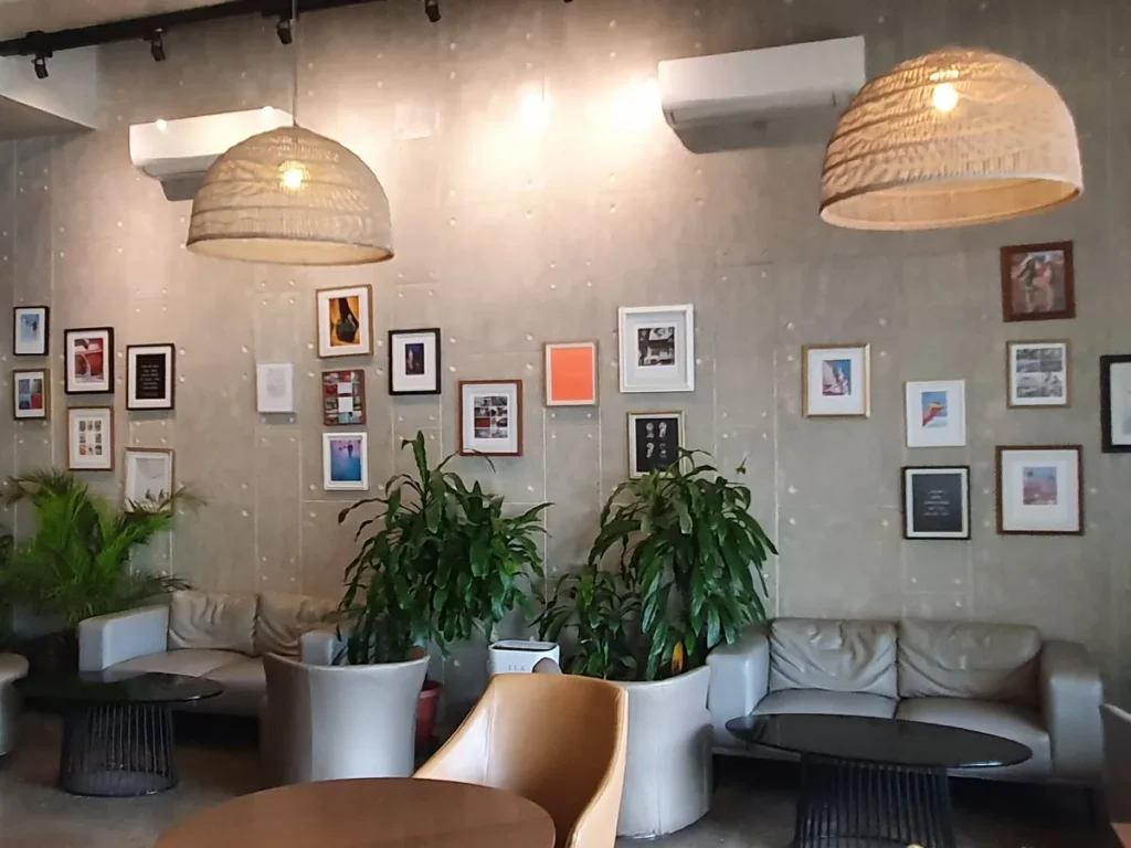 필리핀 세부 셀라(CELLA) 유니캠퍼스 어학원 주변시설 카페로, 라탄 펜던트 조명 두 개와 다양한 액자가 촘촘히 걸린 회색 벽면 소파 좌석입니다.