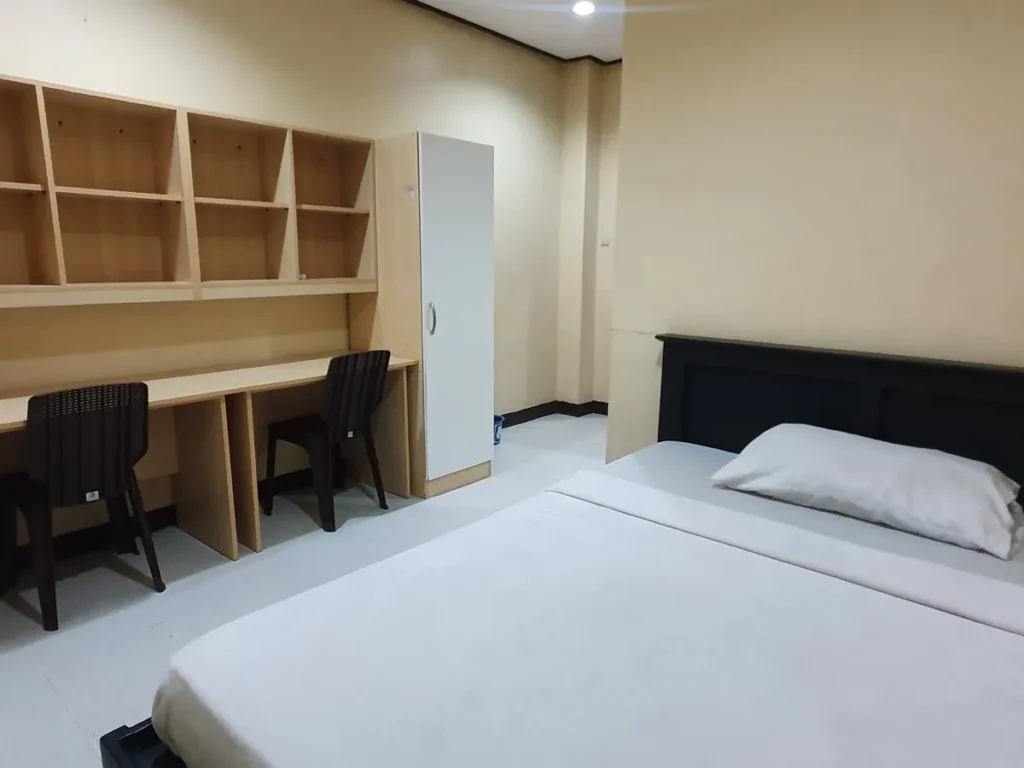 필리핀 세부 CG 바닐라드 어학원 기숙사 1인실로, 좌측 벽선반·책상과 흰색 붙박이장, 우측 짙은 원목 헤드보드의 싱글 침대가 있는 객실 전경입니다.
