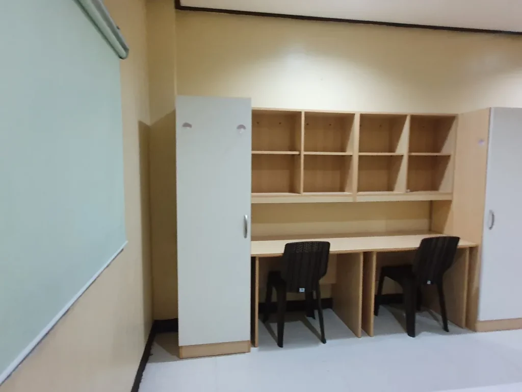 필리핀 세부 CG 바닐라드 어학원 기숙사 1인실로, 벽선반 아래 책상 두 자리와 검정 의자, 옆에 흰색 슬라이드 옷장이 놓인 학습 공간입니다.