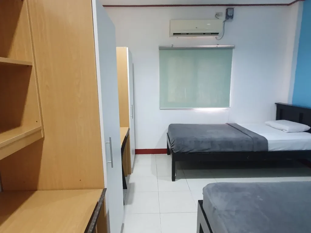 필리핀 세부 CG 바닐라드 어학원 기숙사 2인실로, 원목 책장과 회색 옷장이 놓인 입구 쪽에서 안쪽 침대와 창가 에어컨까지 이어지는 방 구조가 보입니다.
