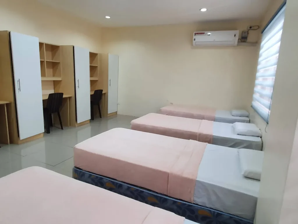 필리핀 세부 CG 바닐라드 어학원 기숙사 4인실로, 왼쪽 책상 겸용 옷장 4세트와 오른쪽 창가 침대들이 함께 보이는 실내 전경입니다.