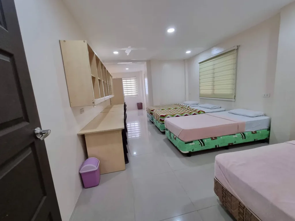 필리핀 세부 CG 바닐라드 어학원 기숙사 4인실로, 줄무늬 이불의 침대 여러 개와 벽면 선반, 분홍 휴지통이 놓인 다른 호실 전경입니다.