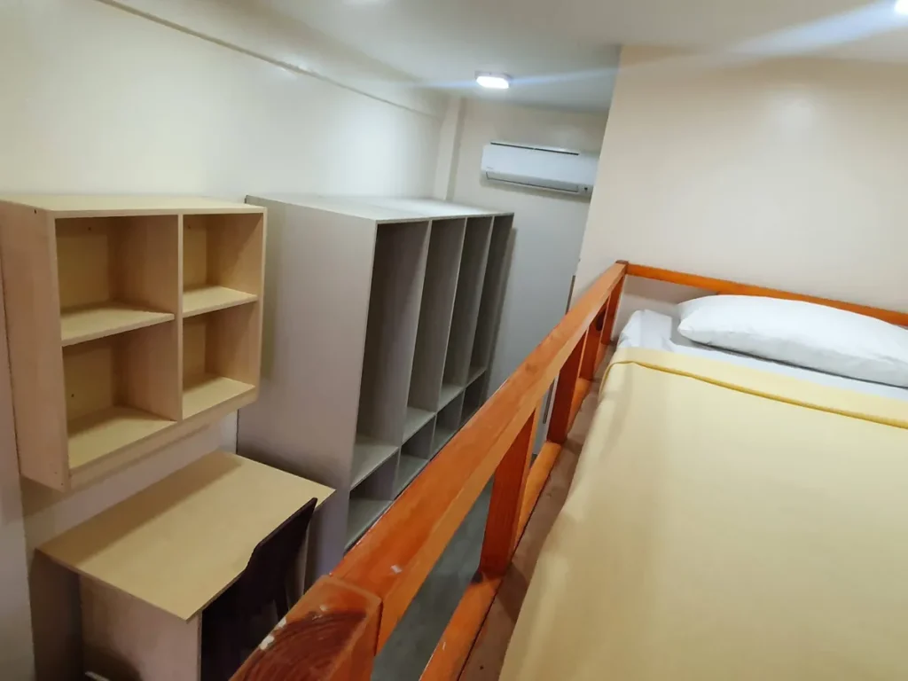 필리핀 세부 CG 바닐라드 어학원 기숙사 4인실(2층침대)로, 2층 침대 위 칸에서 내려다본 벽선반·붙박이장·책상과 벽걸이 에어컨이 보이는 시야입니다.
