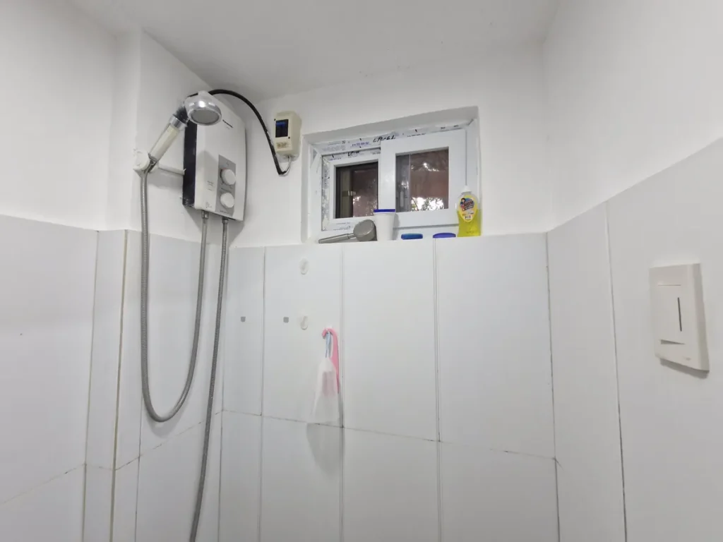 필리핀 세부 CG 바닐라드 어학원 기숙사 4인실(2층침대) 화장실로, 온수기 샤워기와 작은 창문 아래 세면도구가 놓인 샤워 공간입니다.