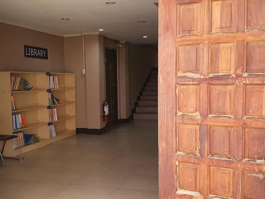 필리핀 세부 CG 바닐라드 어학원 강의실 교재로, LIBRARY 책장과 계단이 보이는 복도 옆에 짙은 원목 문짝이 크게 드러난 모습입니다.
