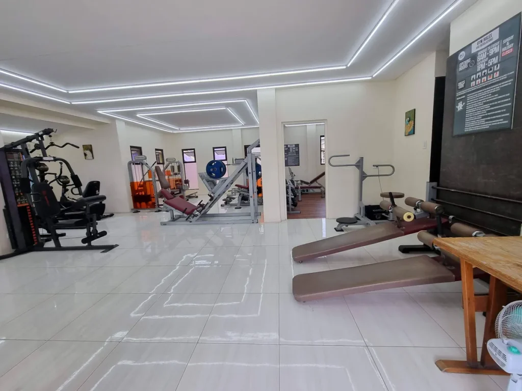 필리핀 세부 CG 바닐라드 어학원 운동시설 헬스장으로, 복합 웨이트 머신과 레그프레스, 짐볼 벤치가 안내판 아래 배치된 실내 전경입니다.