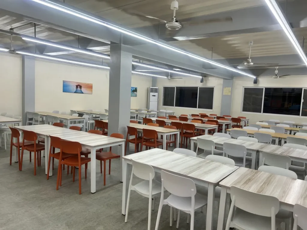 필리핀 세부 CG 바닐라드 어학원 식당으로, 주황색과 화이트 플라스틱 의자가 놓인 테이블들과 벽면 풍경 사진이 보이는 야간 좌석 공간입니다.