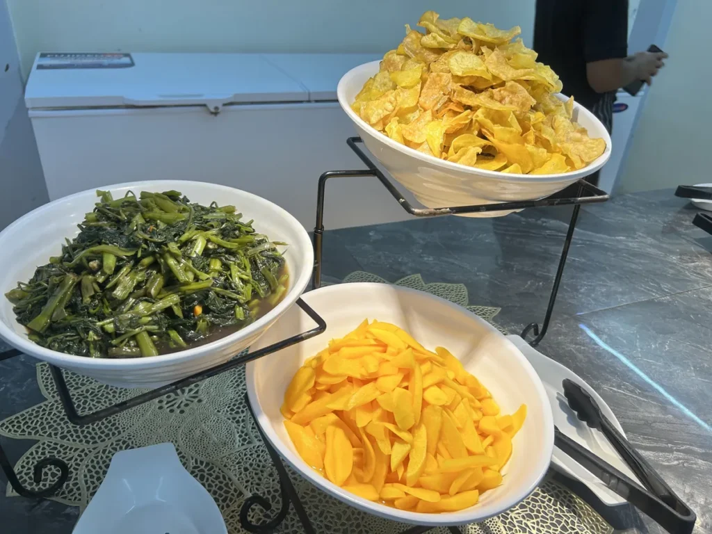 필리핀 세부 CG 바닐라드 어학원 식당 식사로, 3단 거치대에 감자칩·시금치나물·망고가 각각 흰 볼에 담겨 뷔페 라인에 놓여 있습니다.