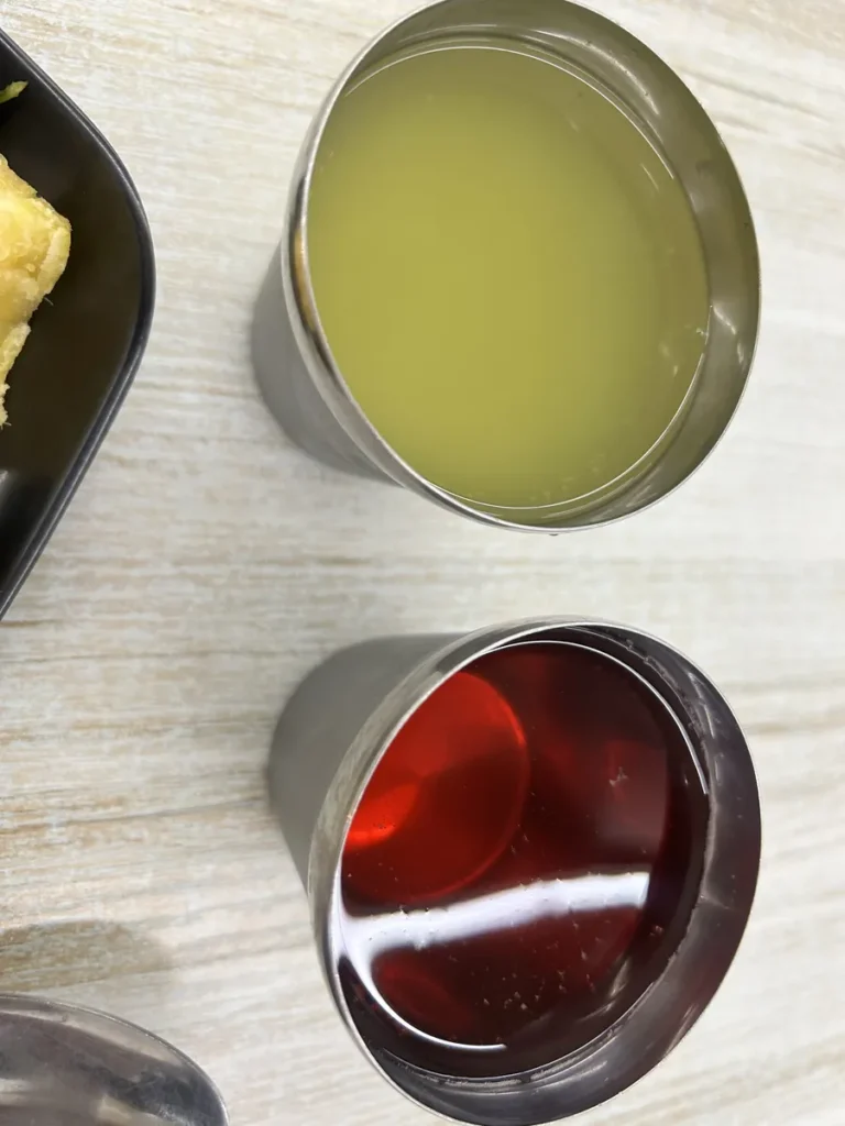 필리핀 세부 CG 바닐라드 어학원 식당 식사로, 스텐 컵 두 개에 연두색 음료와 붉은 음료가 각각 채워진 모습을 위에서 가까이 보여줍니다.