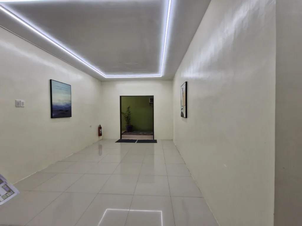 필리핀 세부 CG 바닐라드 어학원 입구로비로, 천장 LED 간접조명 아래 복도에 액자 두 점이 걸려 있고 안쪽으로 초록빛 방 입구가 보입니다.