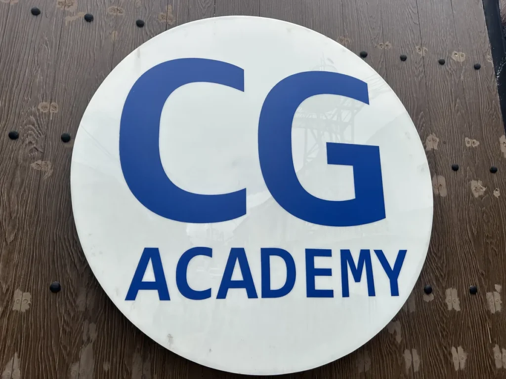 필리핀 세부 CG 바닐라드 어학원 캠퍼스 전경으로, 목재 벽면에 부착된 원형 CG ACADEMY 로고 간판이 보이는 클로즈업입니다.