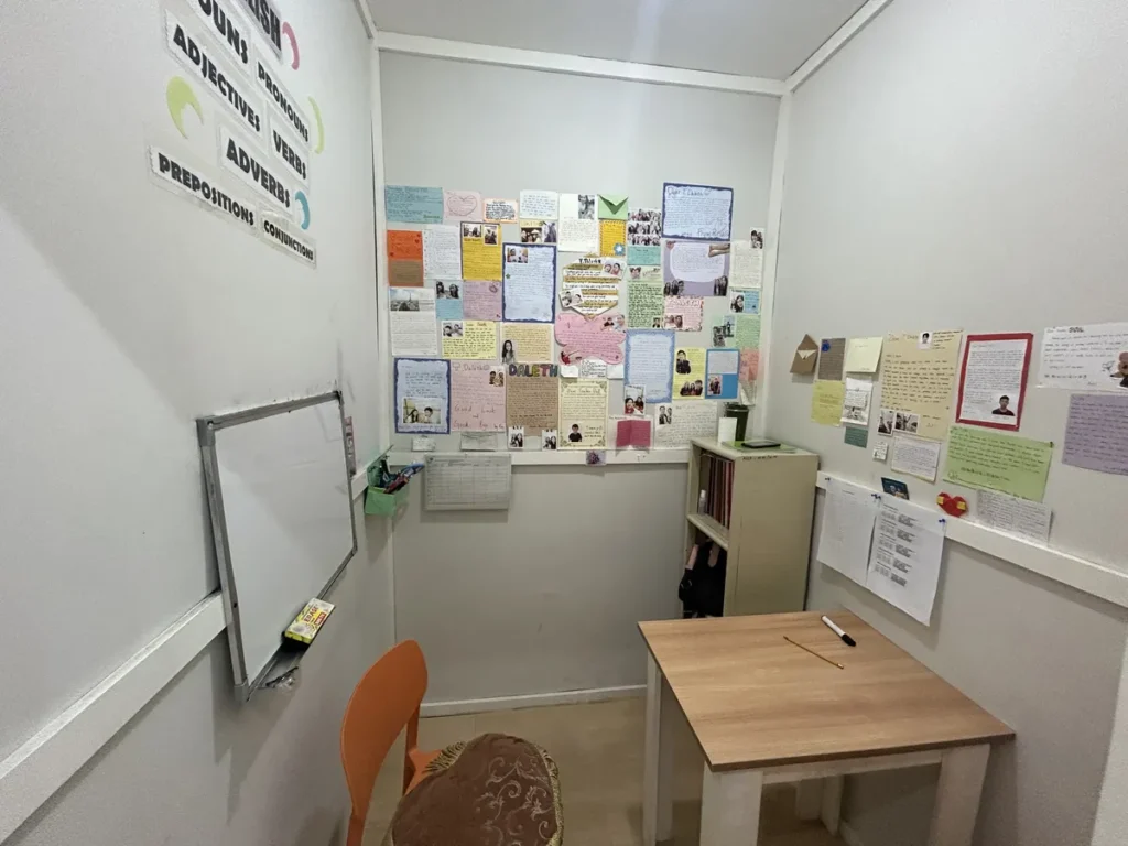필리핀 세부 CG 스파르타 어학원 강의실 일대일 수업실로, 화이트보드와 학생 편지·사진이 빼곡히 붙은 벽, 원목 책상과 의자가 놓인 방 전체 모습입니다.