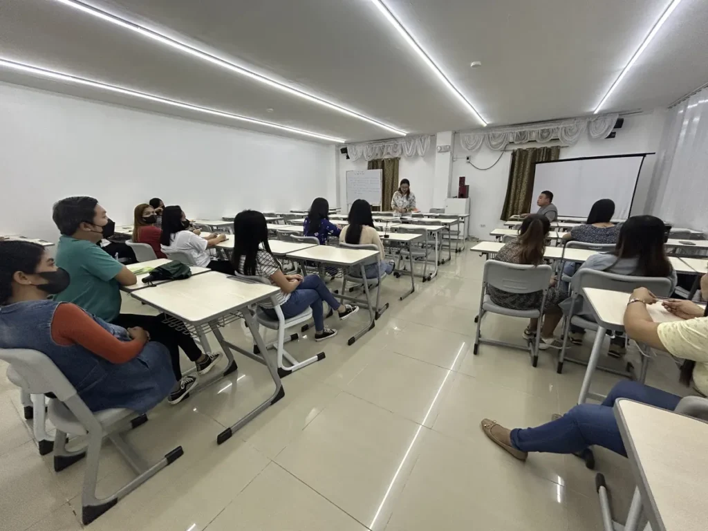 필리핀 세부 CG 스파르타 어학원 강의실 그룹반으로, 마스크를 쓴 학생들이 책상에 앉아 커튼과 스크린이 있는 강의실에서 수업을 듣는 모습입니다.