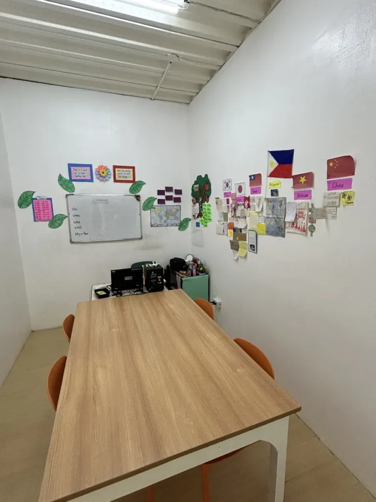 필리핀 세부 CG 스파르타 어학원 강의실 그룹반으로, 각국 국기와 메모가 붙은 벽 아래 원목 테이블과 의자가 놓인 소규모 스터디 공간입니다.