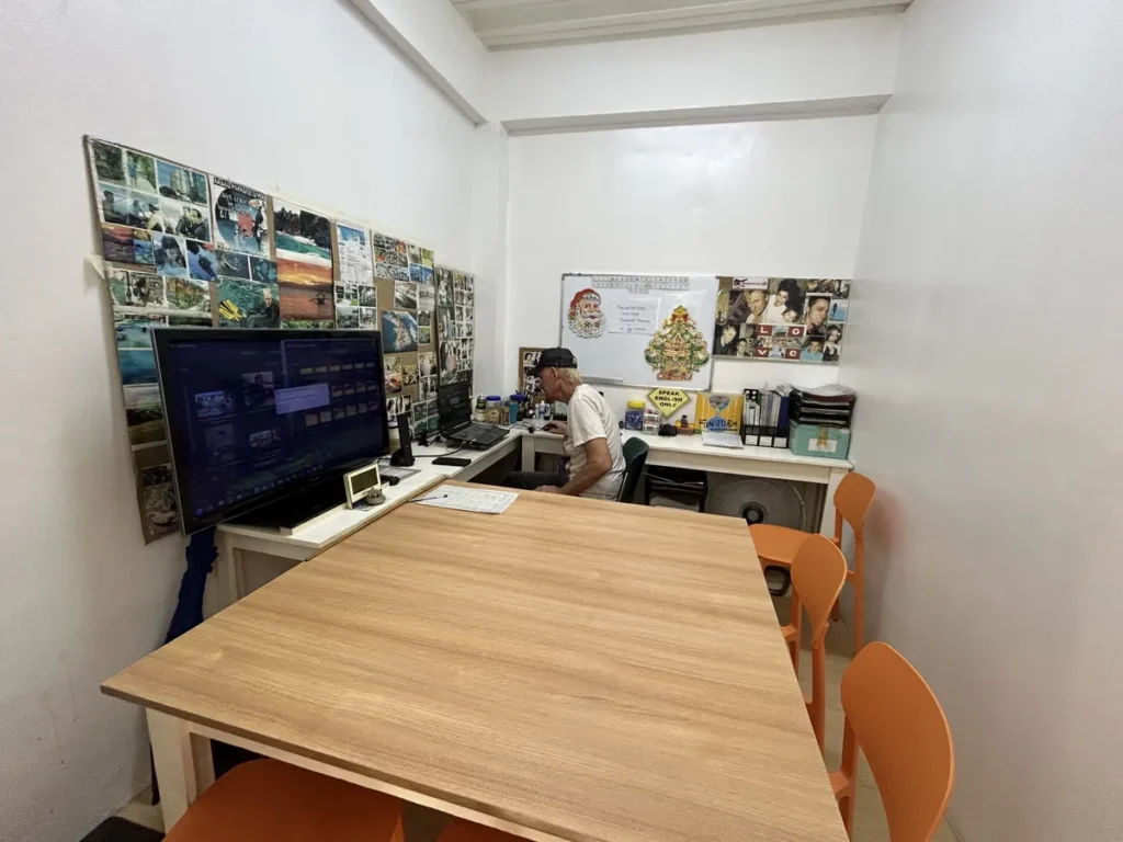필리핀 세부 CG 스파르타 어학원 강의실 그룹반으로, 대형 모니터와 사진들이 붙은 벽 앞에서 선생님이 책상에 앉아 있는 사무 공간입니다.