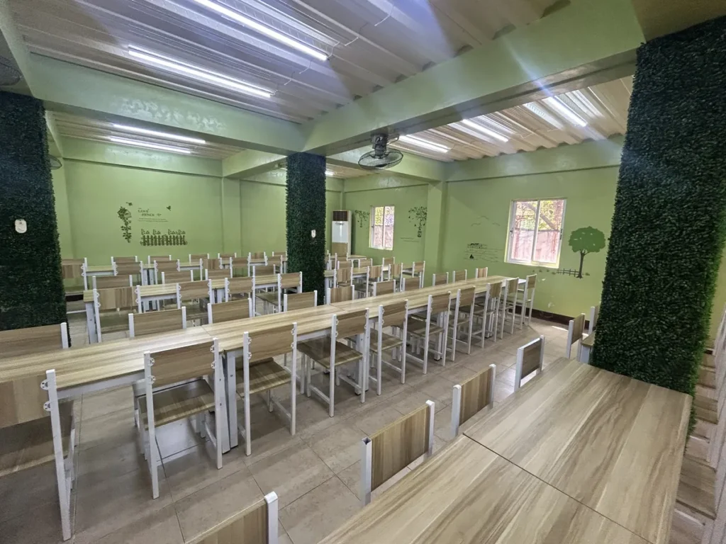 필리핀 세부 CG 스파르타 어학원 식당으로, 초록 담쟁이 기둥 사이 원목 식탁과 의자가 줄지어 놓인 식당 홀입니다.