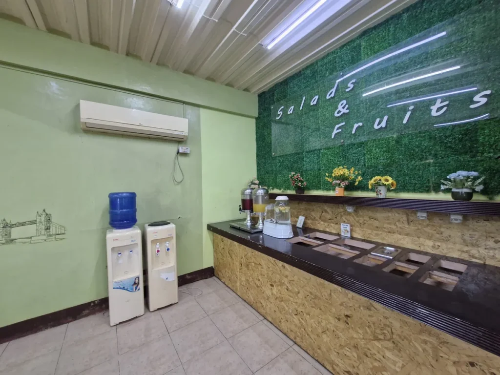 필리핀 세부 CG 스파르타 어학원 식당으로, 'Salads & Fruits' 코너에 정수기와 주스 디스펜서, 생화 장식이 놓인 샐러드바입니다.