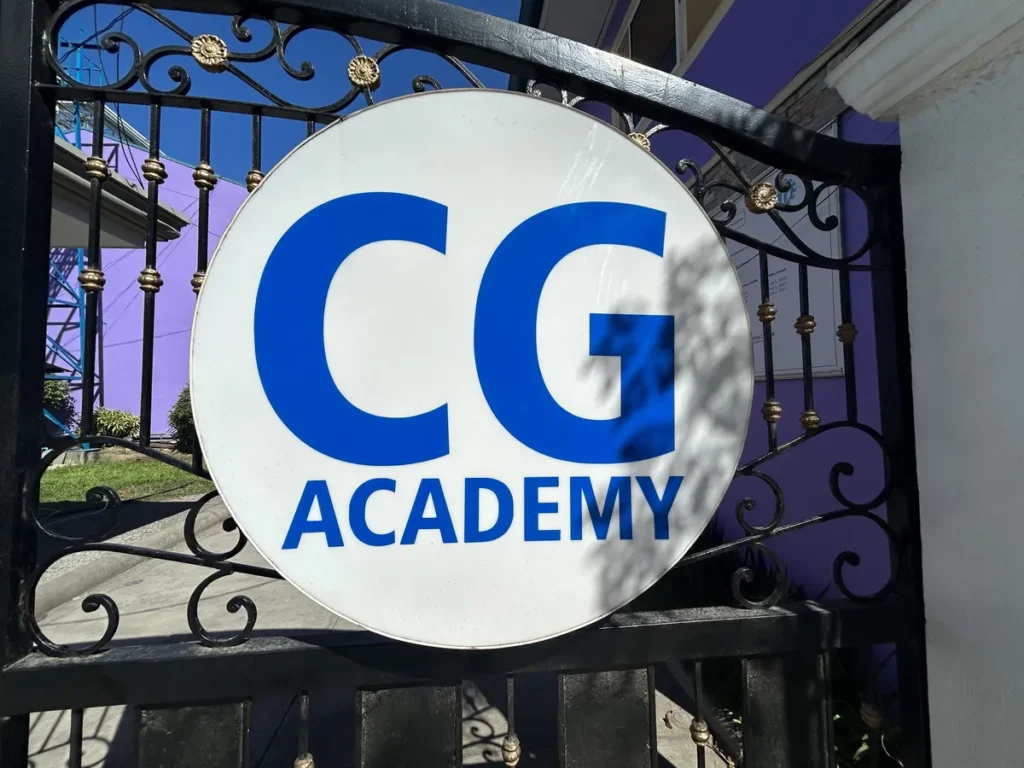 필리핀 세부 CG 스파르타 어학원 학원전경 외관으로, 파란 CG 로고와 ACADEMY 글자가 새겨진 원형 간판이 정문 철제 대문에 부착된 모습입니다.