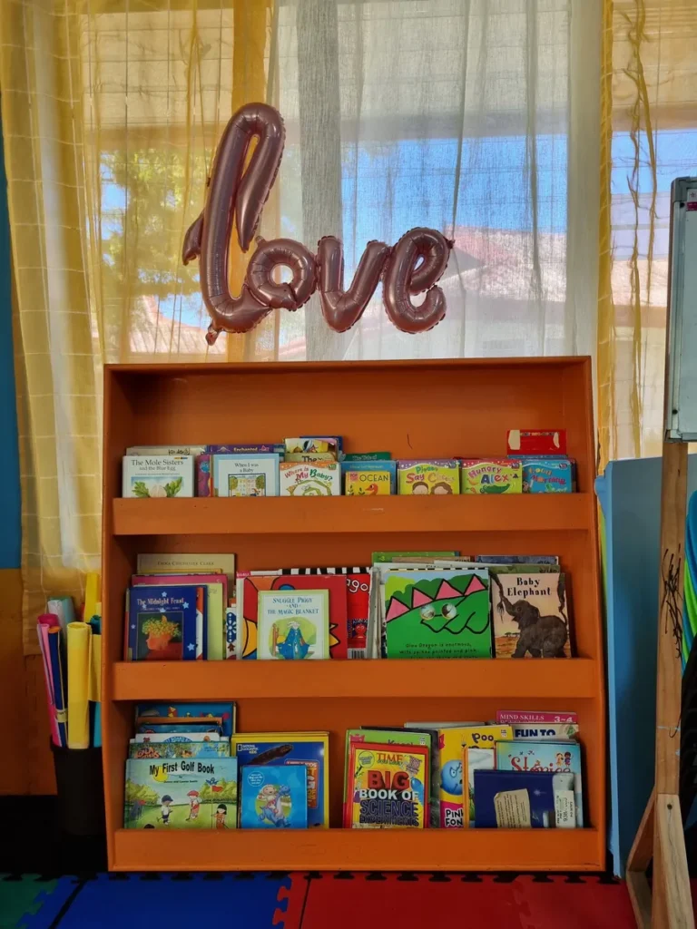 필리핀 세부 엘사(ELSA) 어학원 강의실 키즈룸으로, 'love' 풍선 장식 아래 주황색 책장 세 칸에 영어 그림책이 가득 꽂힌 도서 코너입니다.