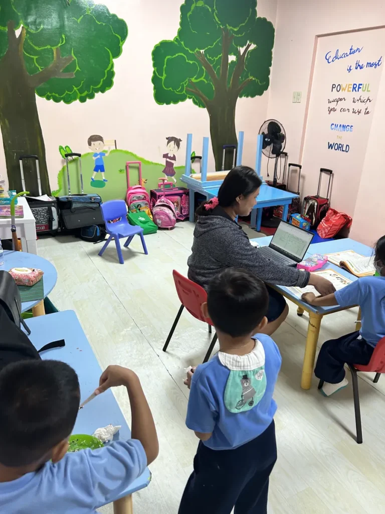 필리핀 세부 엘사(ELSA) 어학원 강의실 키즈룸으로, 나무 벽화가 그려진 분홍빛 교실에서 선생님이 노트북으로 봐주며 아이들이 책상에 앉아 수업받는 모습입니다.