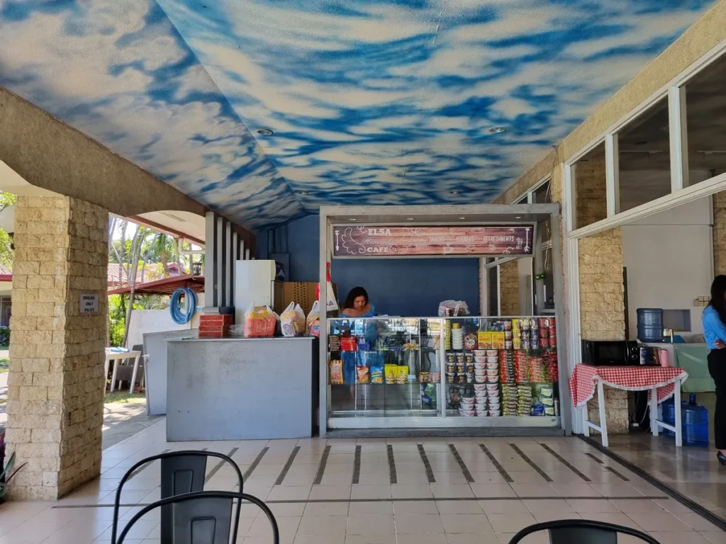 필리핀 세부 엘사(ELSA) 어학원 부대시설 매점으로, 구름 벽화 천장 아래 'ELSA Heavenly Cafe' 간판을 단 매점과 야외 테이블·의자가 놓인 휴게 공간입니다.