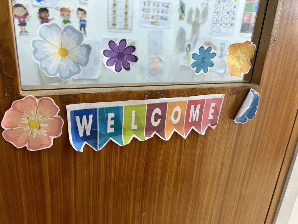 필리핀 세부 엘사(ELSA) 어학원 국제학교 부대시설로, 나무색 문틀에 색색의 종이 꽃 장식과 WELCOME 팻말을 붙여 놓은 환영 장식입니다.