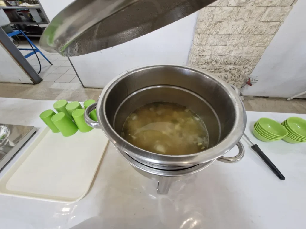 필리핀 세부 엘사(ELSA) 어학원 식당 식사로, 맑은 채소 국물이 담긴 스테인리스 국통과 옆에 쌓인 초록색 컵·그릇이 놓인 국 배식대입니다.