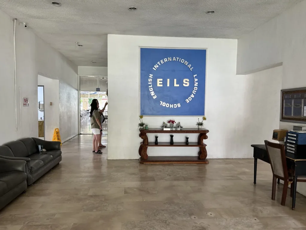 필리핀 세부 엘사(ELSA) 어학원 학원전경 입구로비로, 검정 소파와 콘솔 테이블 위로 EILS 로고 액자가 걸린 로비 공간입니다.